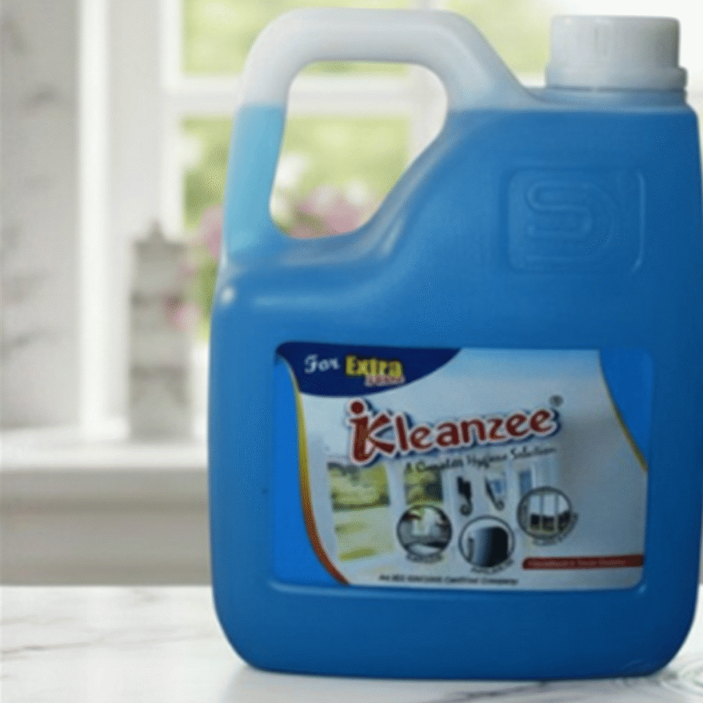 A 5-liter blue gallon container and a 500ml spray bottle of Kleanzee blue liquid glass cleaner on a white marble surface in front of a bright window.