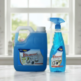 A 5-liter blue gallon container and a 500ml spray bottle of Kleanzee blue liquid glass cleaner on a white marble surface in front of a bright window.