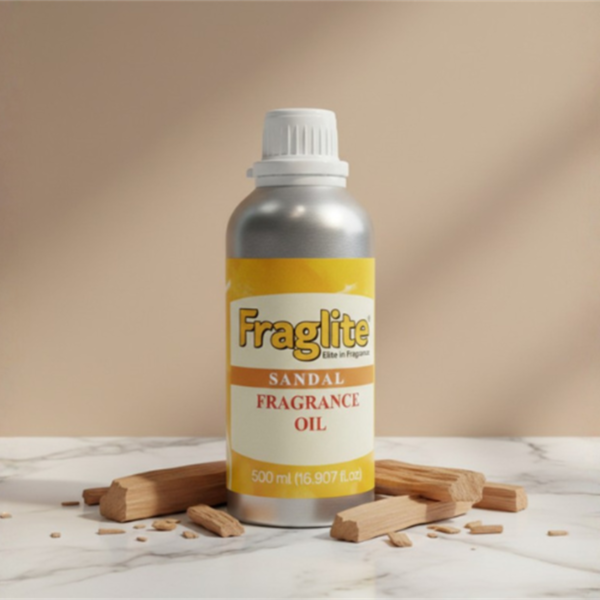 A silver Fraglite bottle with a yellow "Sandal Fragrance Oil" label, centered on a white marble surface surrounded by pieces of natural sandalwood.