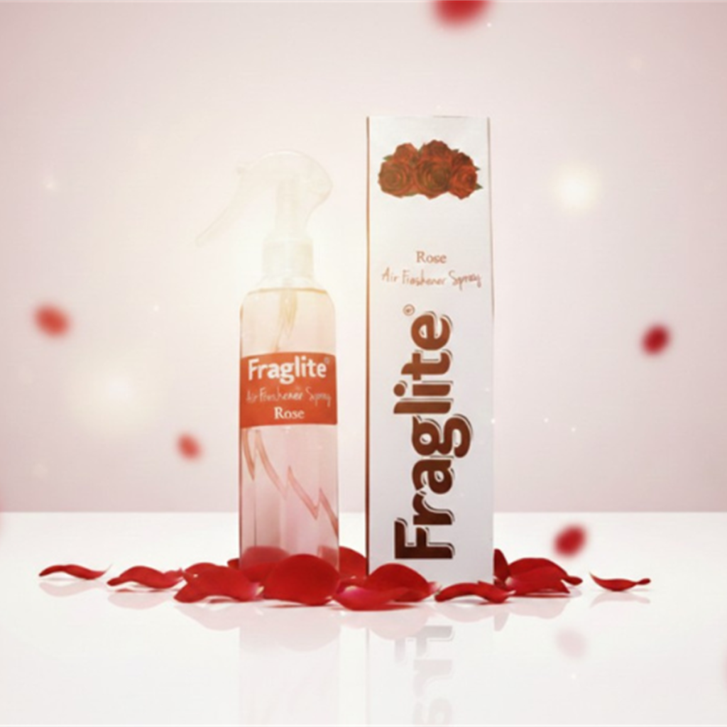 A Fraglite Rose air freshener bottle and box centered against a soft pink background with falling red rose petals.