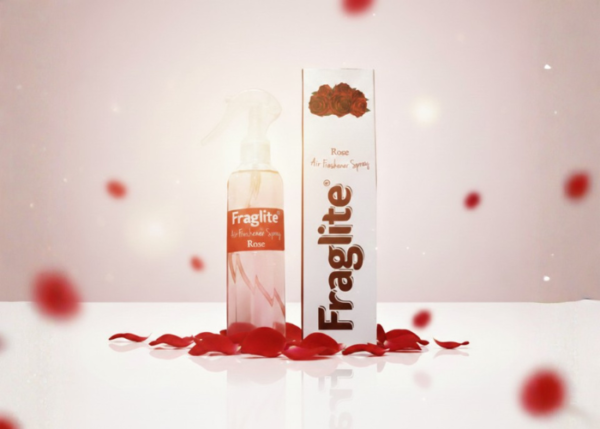 A Fraglite Rose air freshener bottle and box centered against a soft pink background with falling red rose petals.