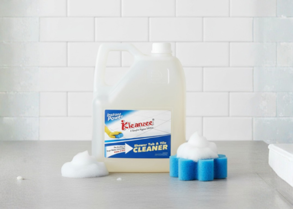 A large, clear plastic gallon jug with a white handle and Kleanzee label, featuring cleaning foam and a blue flower-shaped sponge on a marble countertop.