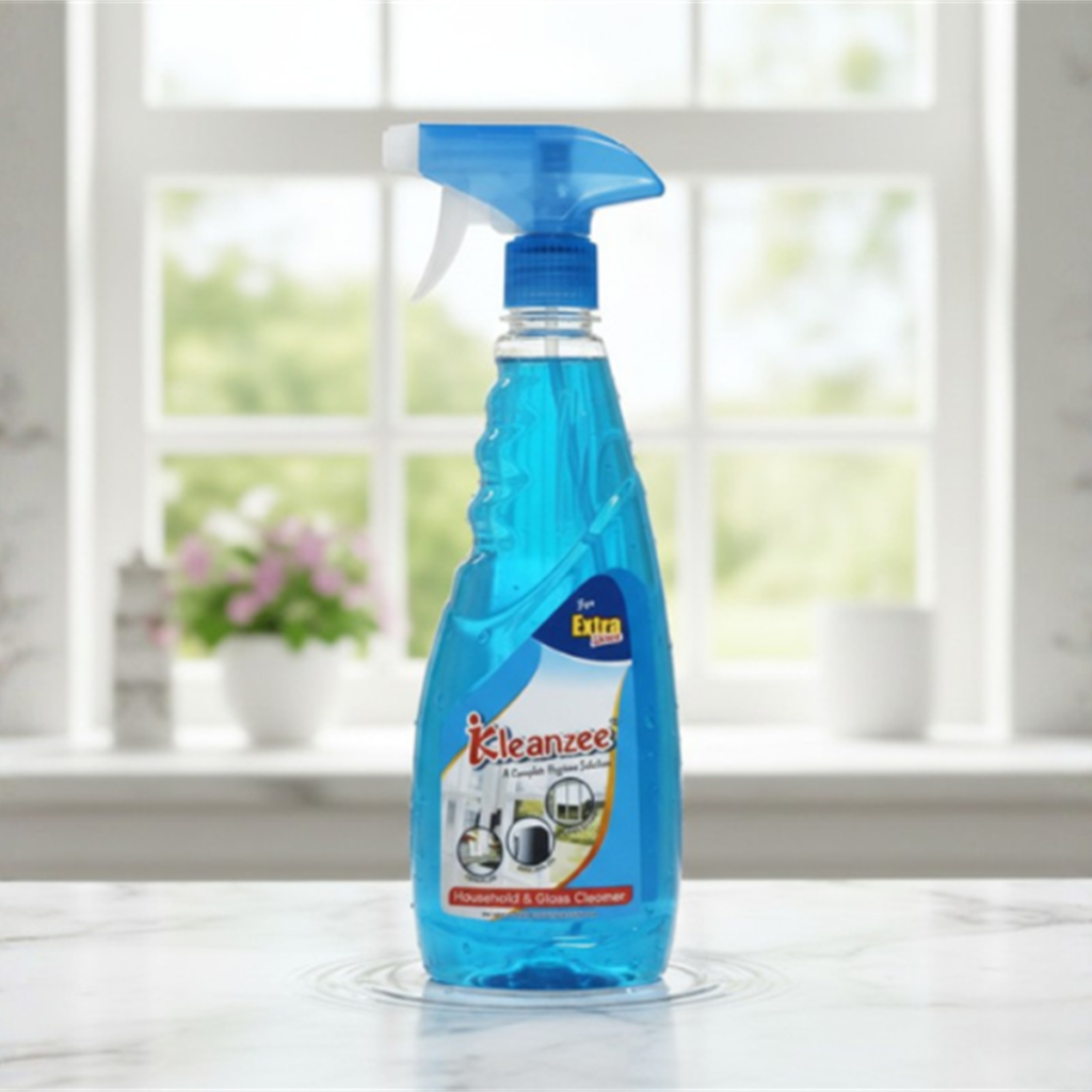 A clear spray bottle filled with blue Kleanzee glass cleaner liquid, standing on a marble countertop with a blurred window and garden background.