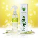 A clear bottle of Fraglite Lemon Grass spray and its box against a vibrant yellow bokeh background with fresh lemongrass stalks at the base.