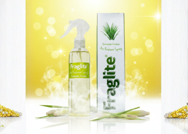 A clear bottle of Fraglite Lemon Grass spray and its box against a vibrant yellow bokeh background with fresh lemongrass stalks at the base.