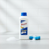 A single white bottle of Kleanzee Shower Tub & Tile Cleaner with a blue cap, positioned on a grey surface with a mound of foam and a blue sponge.