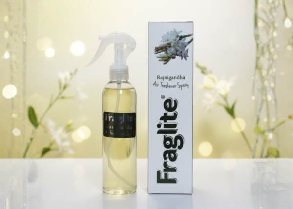 A Fraglite Rajnigandha spray bottle and box set against a soft, glowing background with white tuberose flowers.