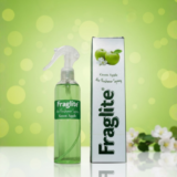 A green Fraglite spray bottle and box against a soft green background with green apples and white apple blossoms.
