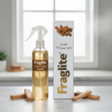 A Fraglite Sandal spray bottle and box on a marble counter with sandalwood sticks scattered around the base.