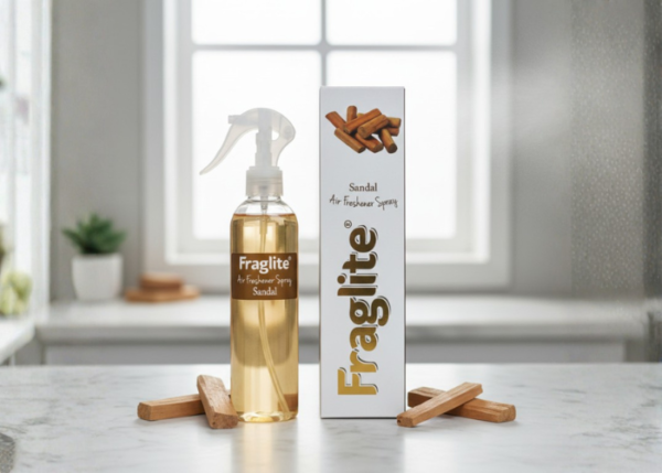 A Fraglite Sandal spray bottle and box on a marble counter with sandalwood sticks scattered around the base.