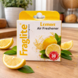 Fraglite Lemon Air Freshener box on a wooden kitchen table surrounded by fresh lemon slices and green leaves.