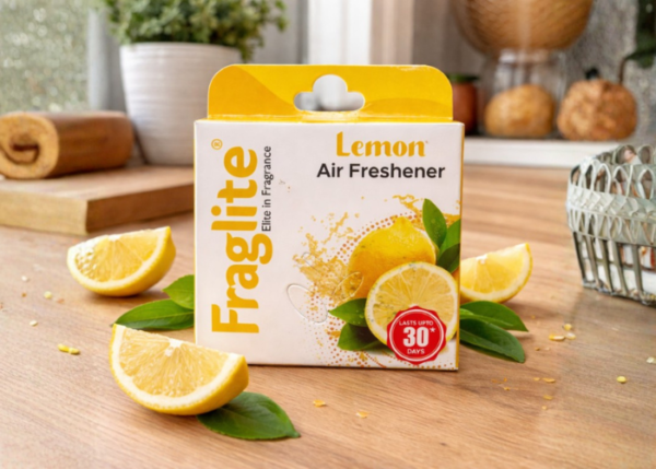 Fraglite Lemon Air Freshener box on a wooden kitchen table surrounded by fresh lemon slices and green leaves.