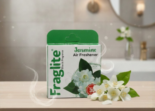 A box of Fraglite Jasmine Air Freshener sitting on a wooden surface next to fresh white jasmine flowers in a bright bathroom setting.